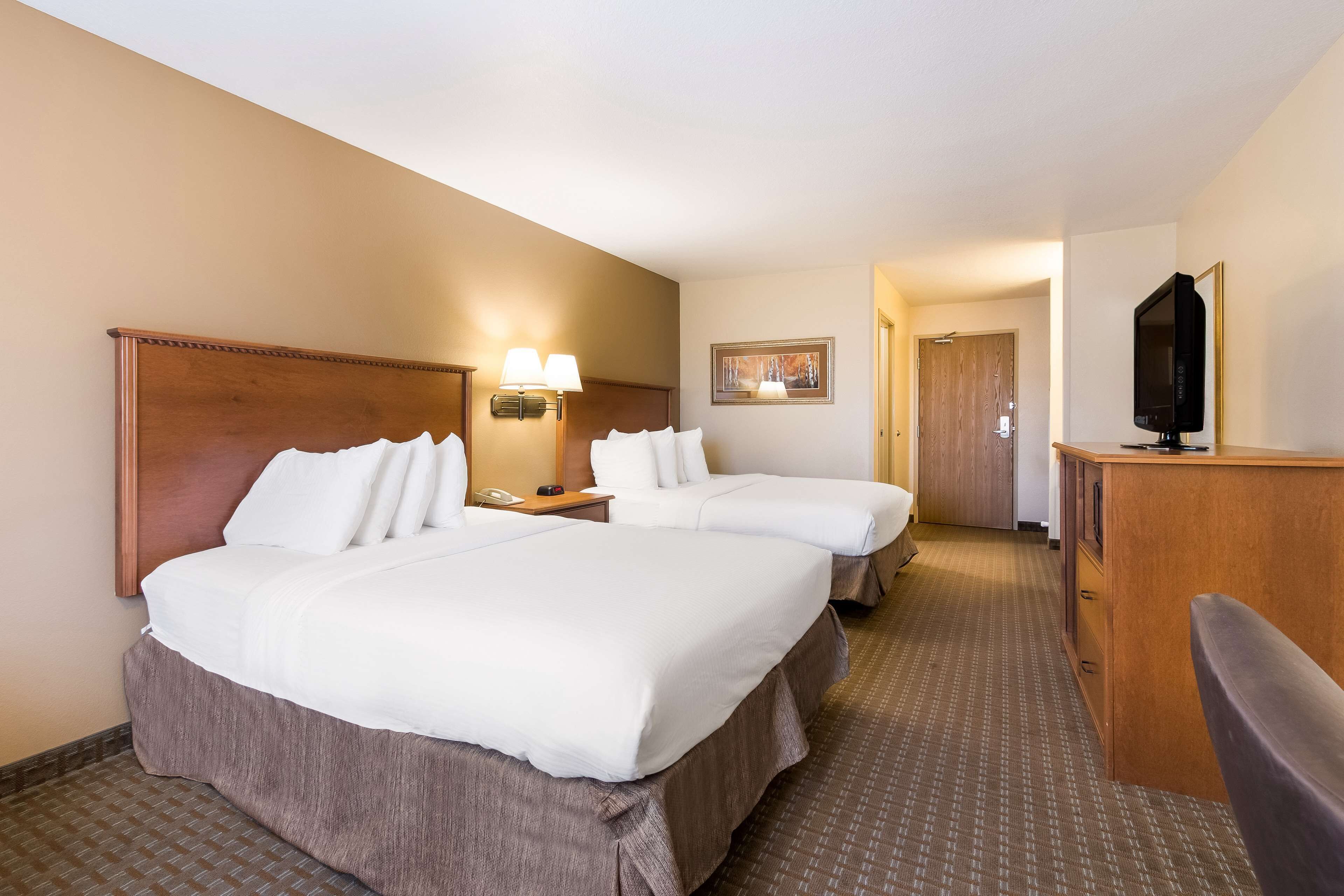 A hotel room with two beds, a desk, a television, and a painting on the wall.