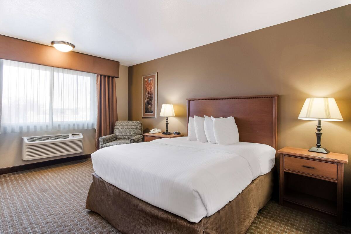 Une chambre d’hôtel avec un grand lit, deux tables de chevet avec des lampes, une chaise, un climatiseur fixé au mur et une fenêtre avec des rideaux.