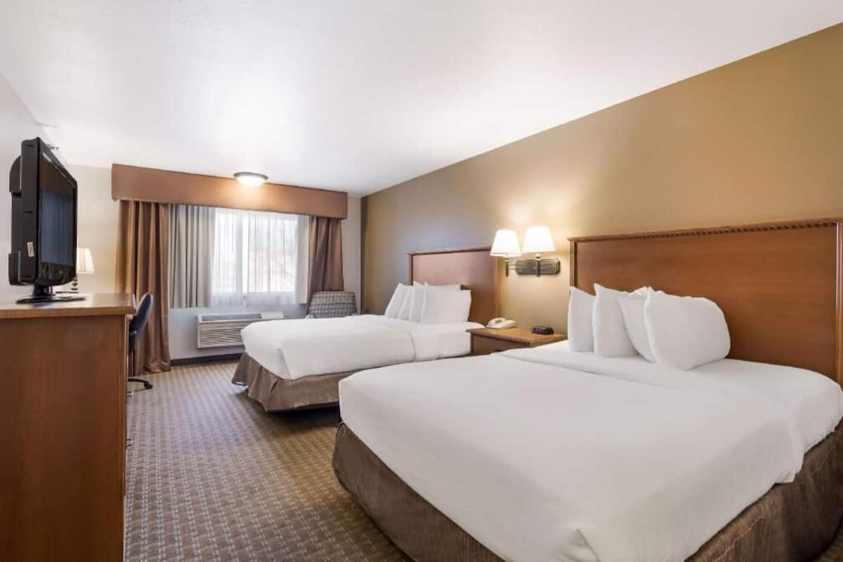 Une chambre d’hôtel avec deux lits, un bureau, une télévision, une lampe et une fenêtre avec des rideaux.