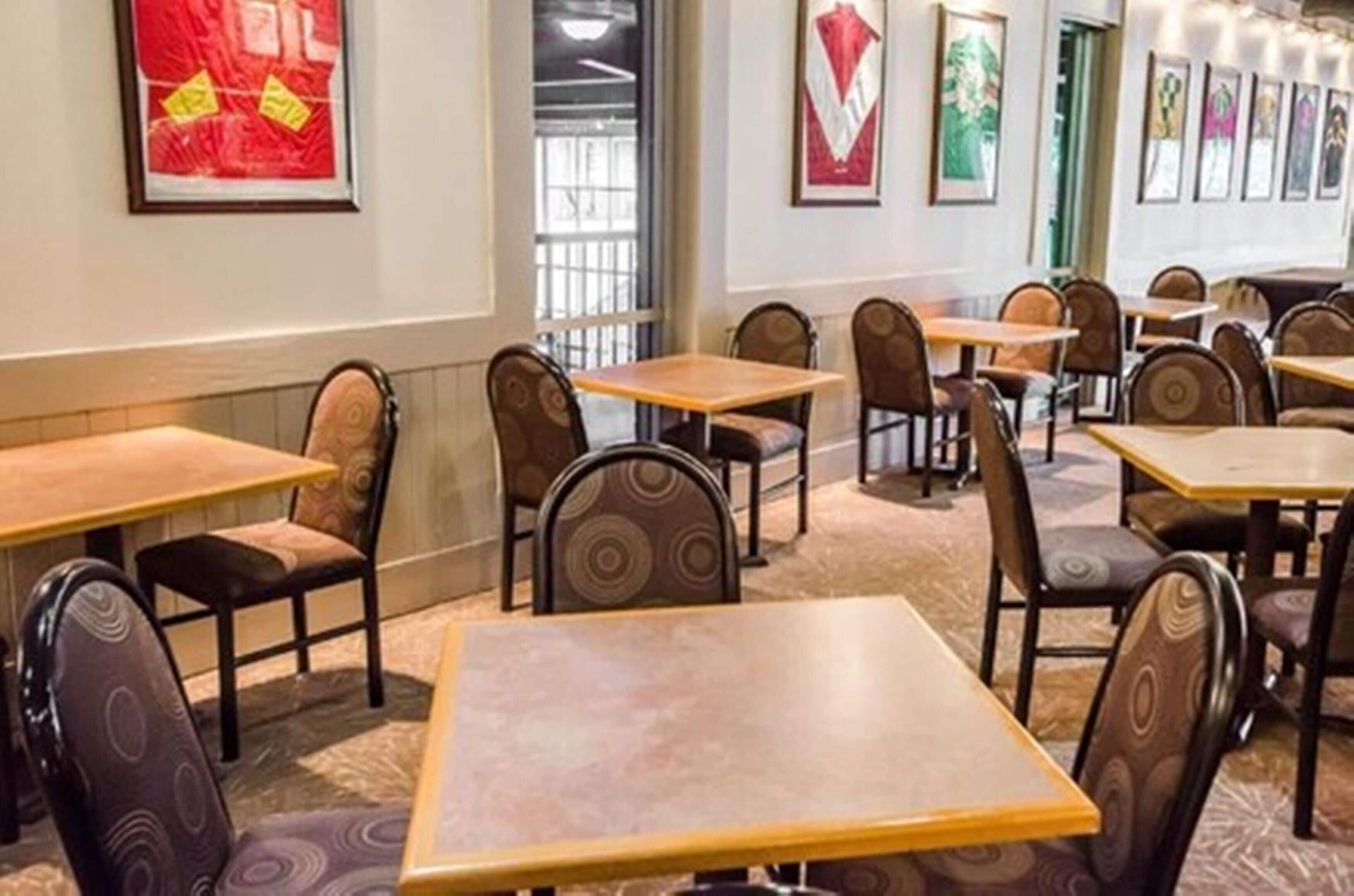 A restaurant with multiple tables and chairs, framed artwork on the walls, and a patterned carpet.