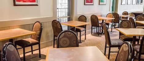 A restaurant with multiple tables and chairs, framed artwork on the walls, and a patterned carpet.