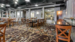 A spacious dining area with multiple tables and chairs, a patterned carpet, and modern lighting fixtures. - Radisson Hotel Louisville North (Clarksville)