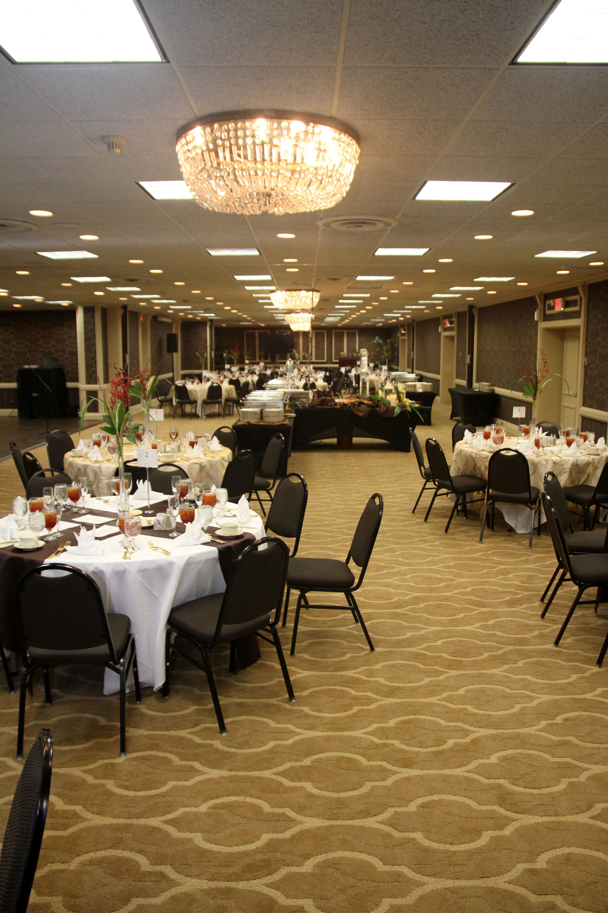 Un salón de banquetes con varias mesas redondas dispuestas para cenar, equipado con sillas y vajilla.