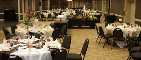Un salón de banquetes con varias mesas redondas dispuestas para cenar, equipado con sillas y vajilla.