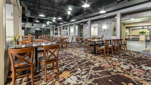 Un restaurant spacieux, doté de nombreuses tables et chaises, d’un tapis à motifs et d’un plafond haut éclairé par des luminaires industriels.