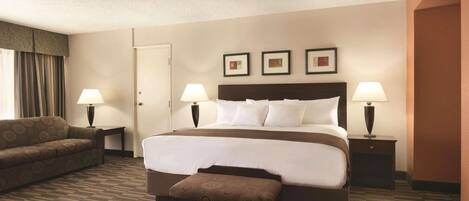 Una habitación de hotel con una cama grande, dos lámparas de noche, un sofá y una pequeña mesa.