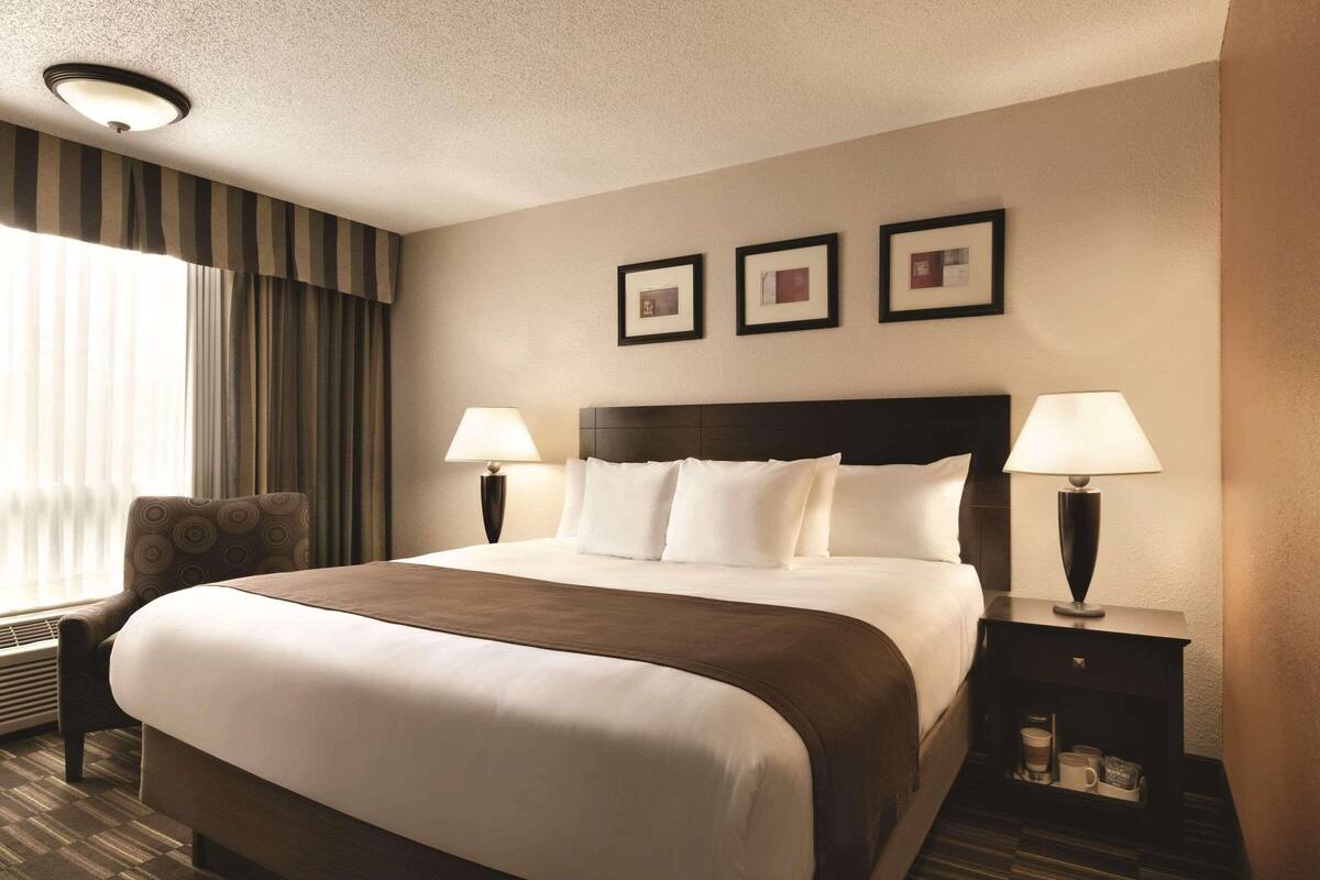 Ein Hotelzimmer mit einem großen Bett, zwei Nachttischen mit Lampen, einem Sessel und einem Fenster mit Vorhängen.