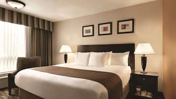 A hotel room with a large bed, two bedside tables with lamps, a chair, and a window with curtains.
