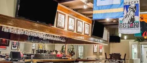 Una zona de bar con mostrador, taburetes y cuadros en la pared.