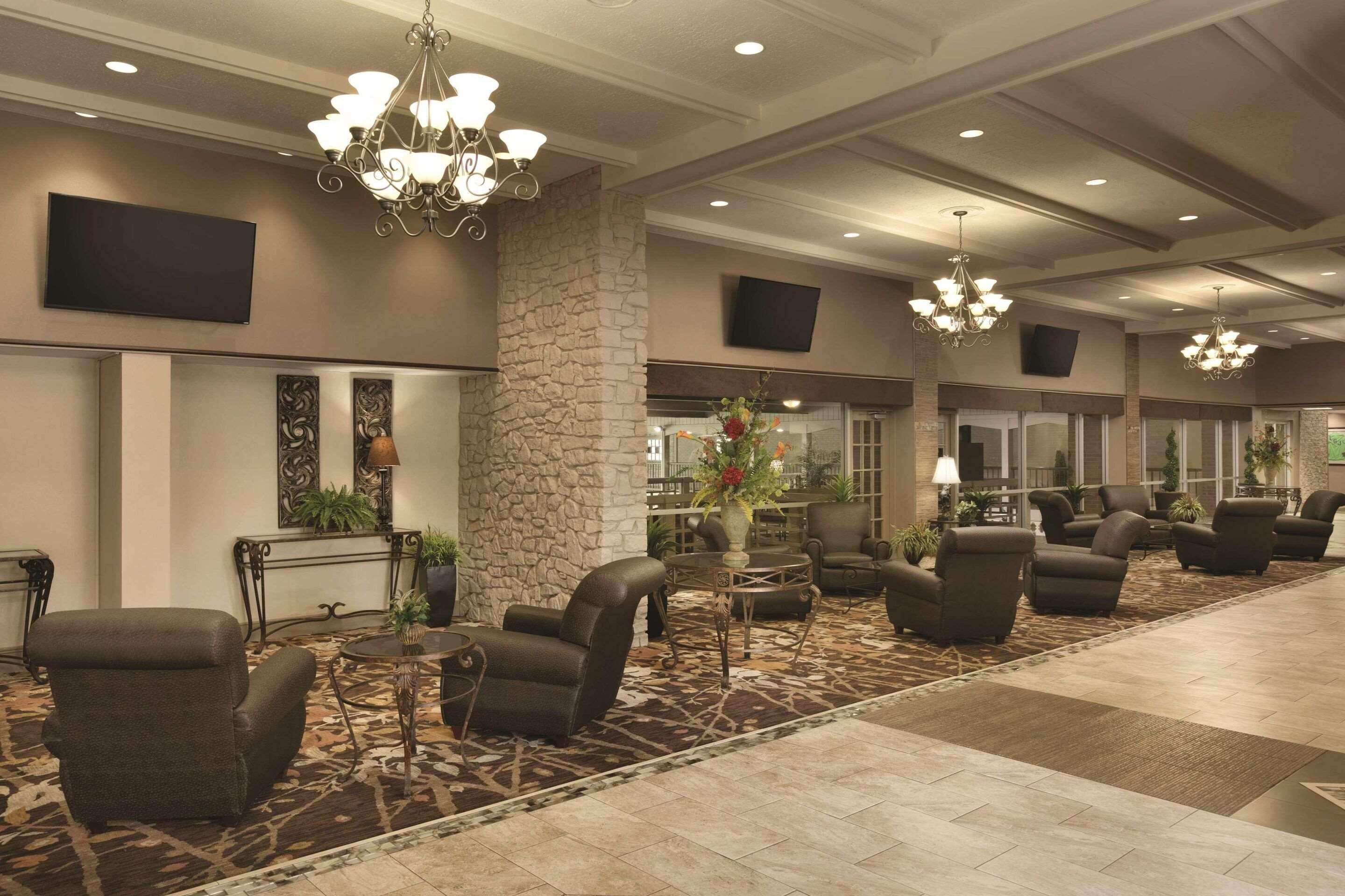 A spacious lobby with multiple seating areas, a stone accent wall, and modern chandeliers.