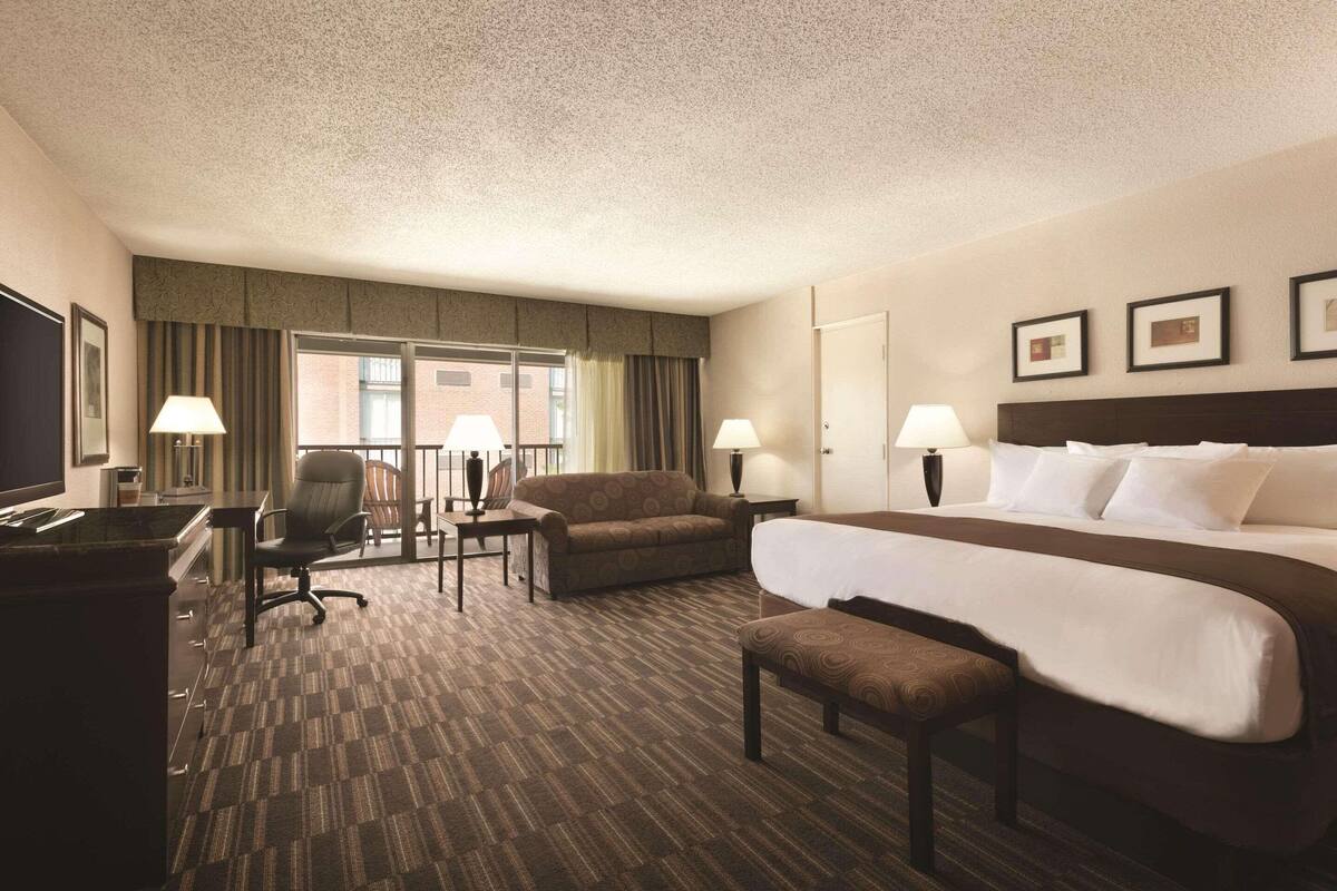 Ein Hotelzimmer mit einem großen Bett, einem Schreibtisch, einem Sessel, einer Couch und einem Fernseher.