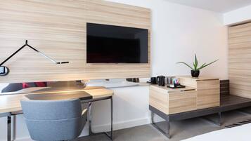 Habitación de hotel moderna con escritorio, silla, televisor de pantalla plana, mesita de noche y una planta en maceta.