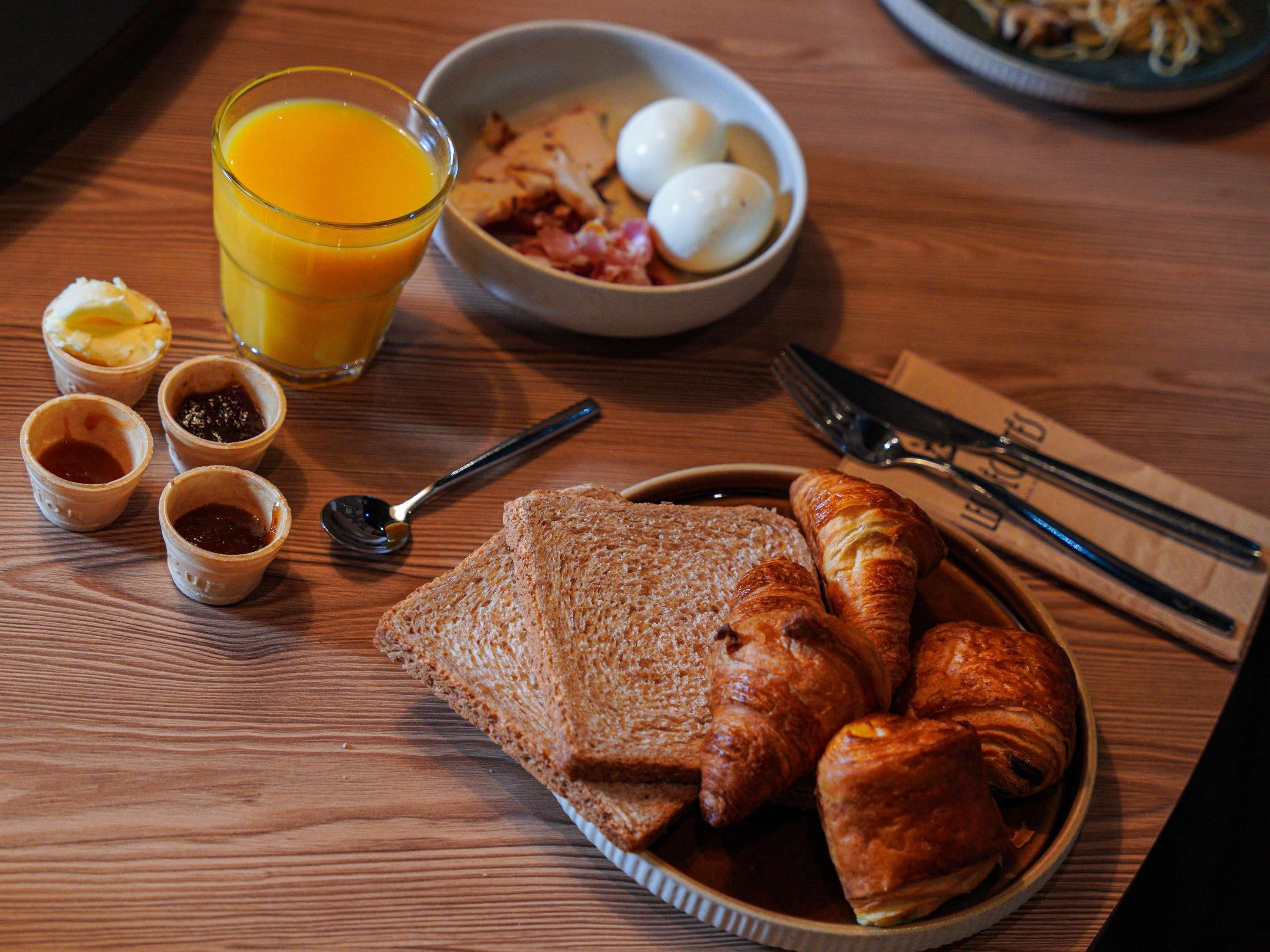 A breakfast setting with bread, croissants, eggs, and orange juice on a wooden table.