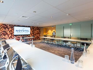 A conference room with a long table, chairs, a screen displaying 'NOVOTEL BORDOAX CENTRE', and a patterned wall. - Novotel Bordeaux Centre-Ville (Bordeaux)