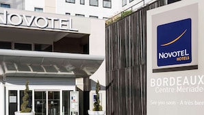 A Novotel hotel entrance with a modern facade, glass doors, and potted plants. - Novotel Bordeaux Centre-Ville (Bordeaux)