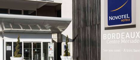 A Novotel hotel entrance with a modern facade, glass doors, and potted plants.