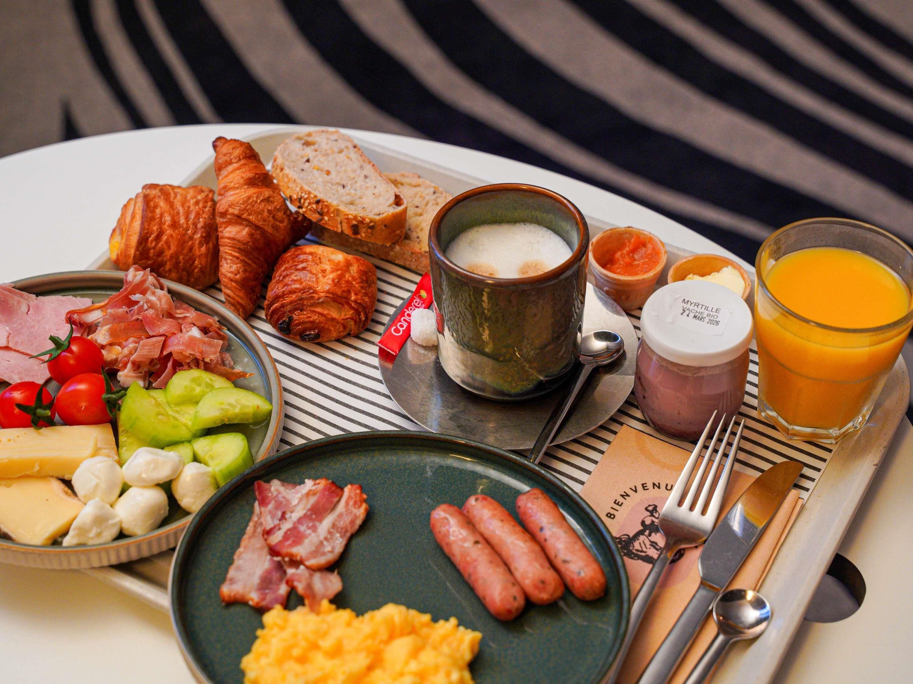 A breakfast tray with croissants, ham, cheese, tomatoes, and a glass of orange juice.