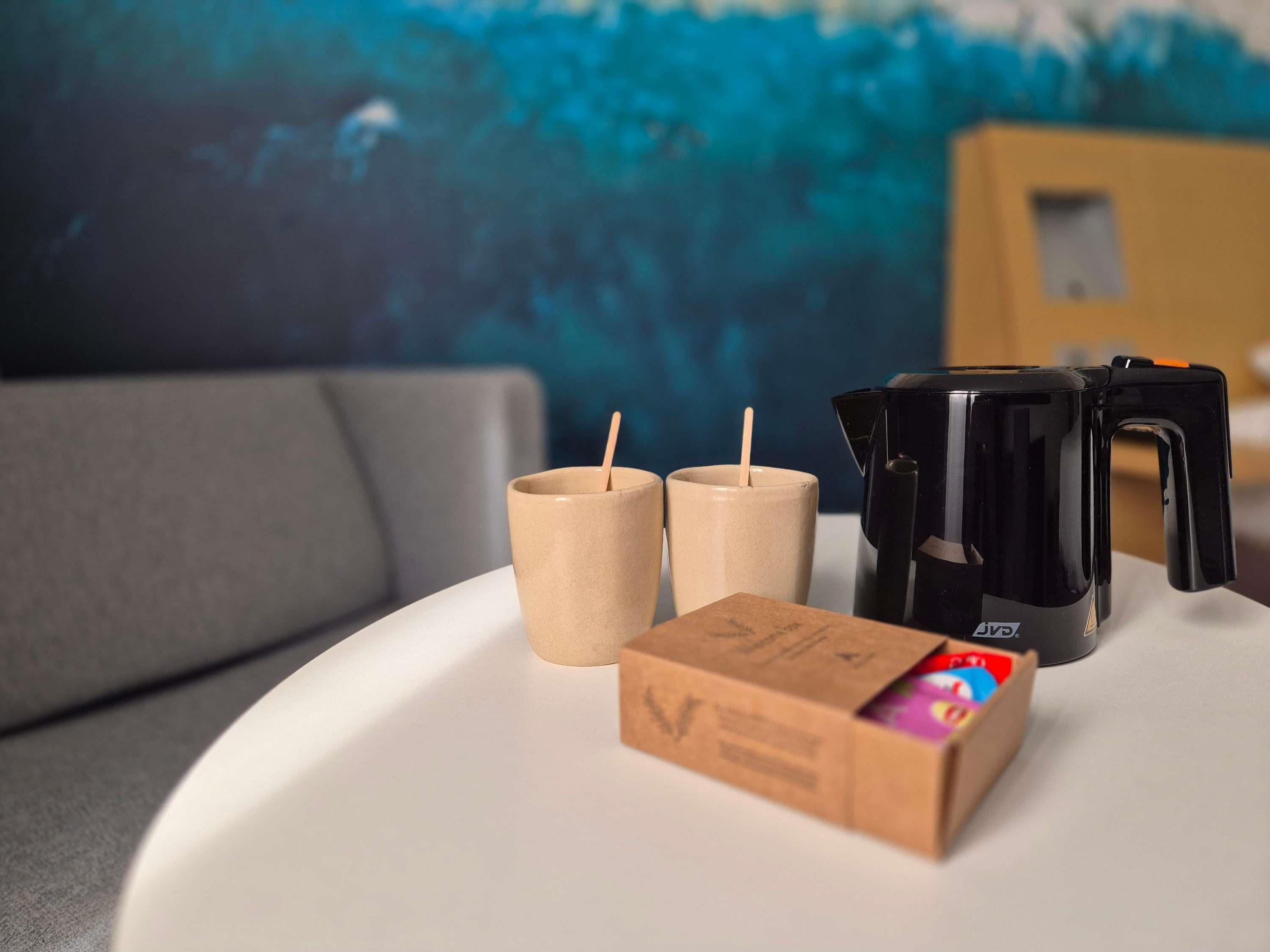 A white table with a black coffee maker, two wooden cups, and a cardboard box with a logo.