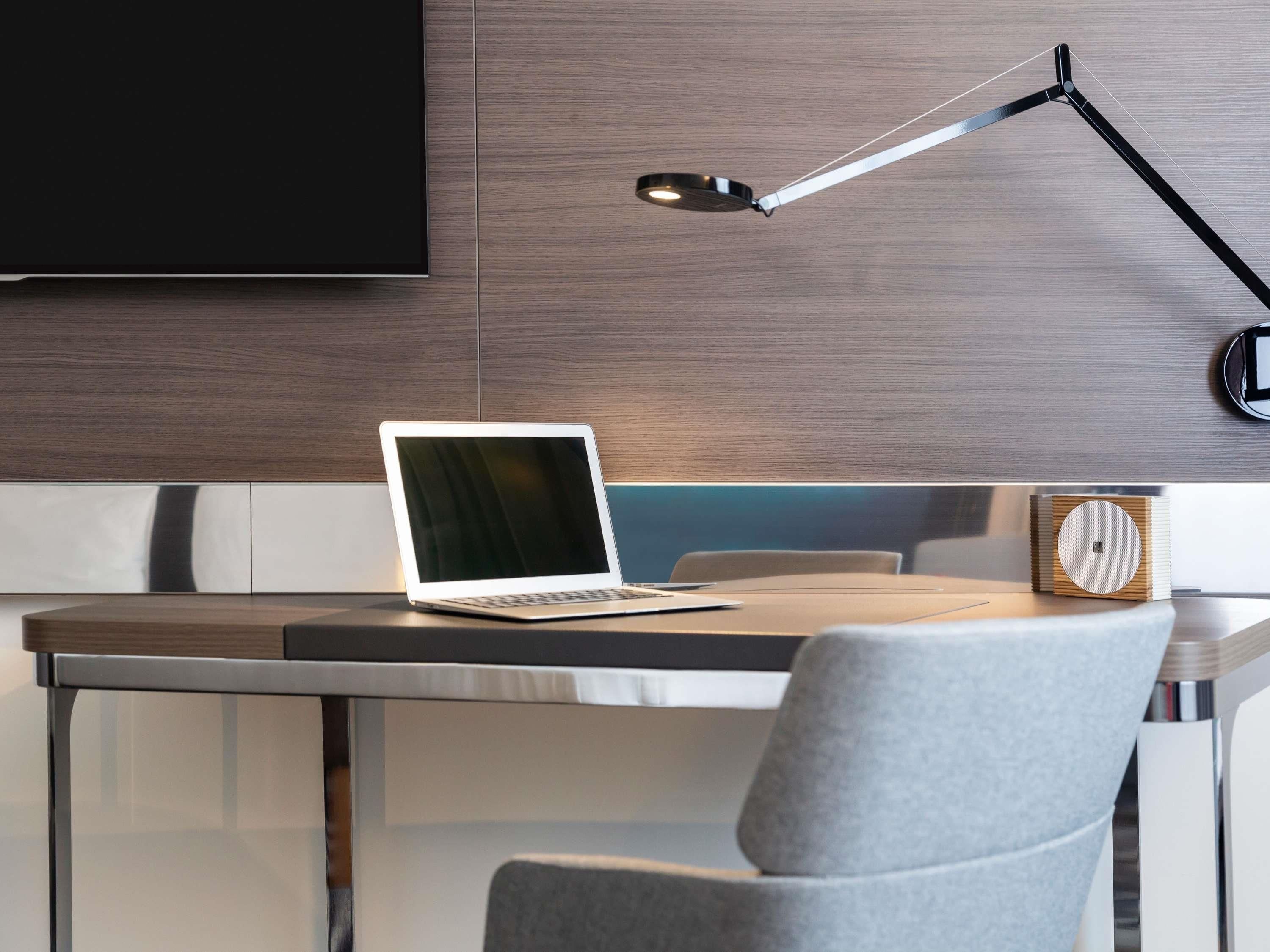 Un espacio de trabajo moderno con una computadora portátil, una lámpara de escritorio y un altavoz.