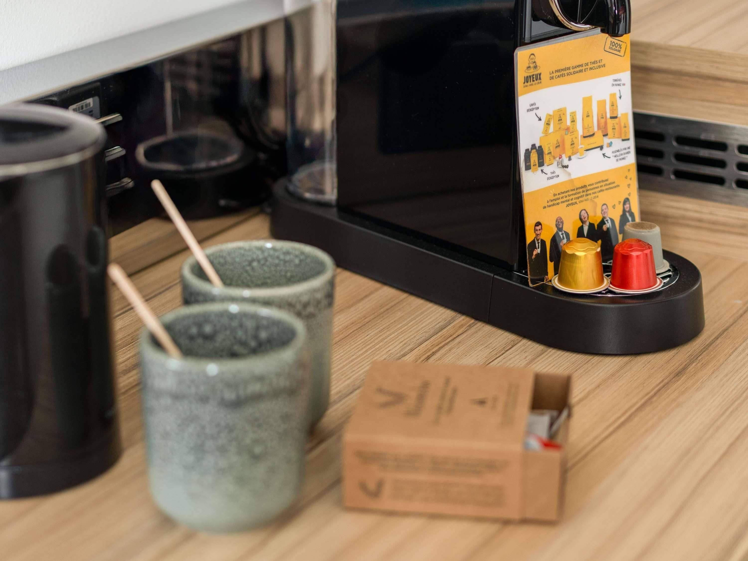A kitchen area with a microwave, two ceramic mugs, a box, and a promotional stand with a yellow label.