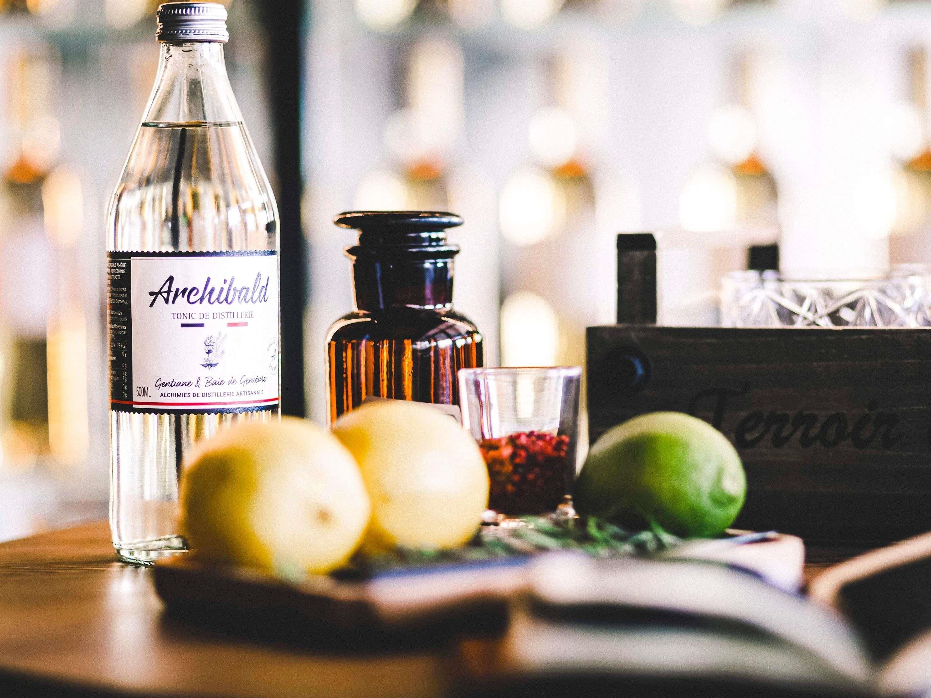 A bottle of Archibold tonic water, lemons, a glass with berries, and a wooden crate with the word 'Terroir' on it.