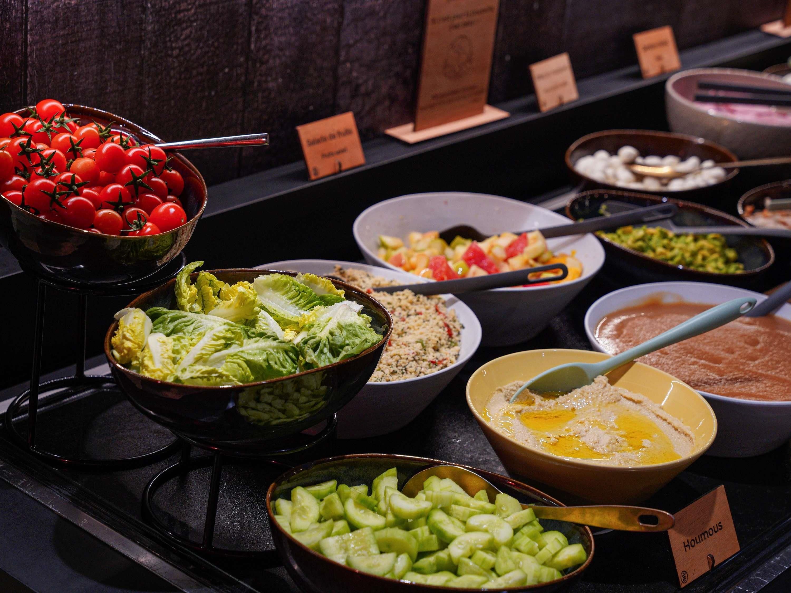 Un buffet con diversi cibi, tra cui pomodori, lattuga e una ciotola di hummus.