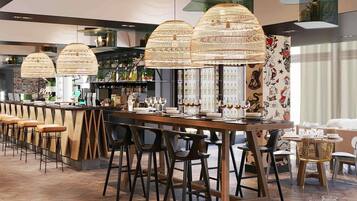 A bar area with wooden bar stools, a long counter, and hanging woven light fixtures.