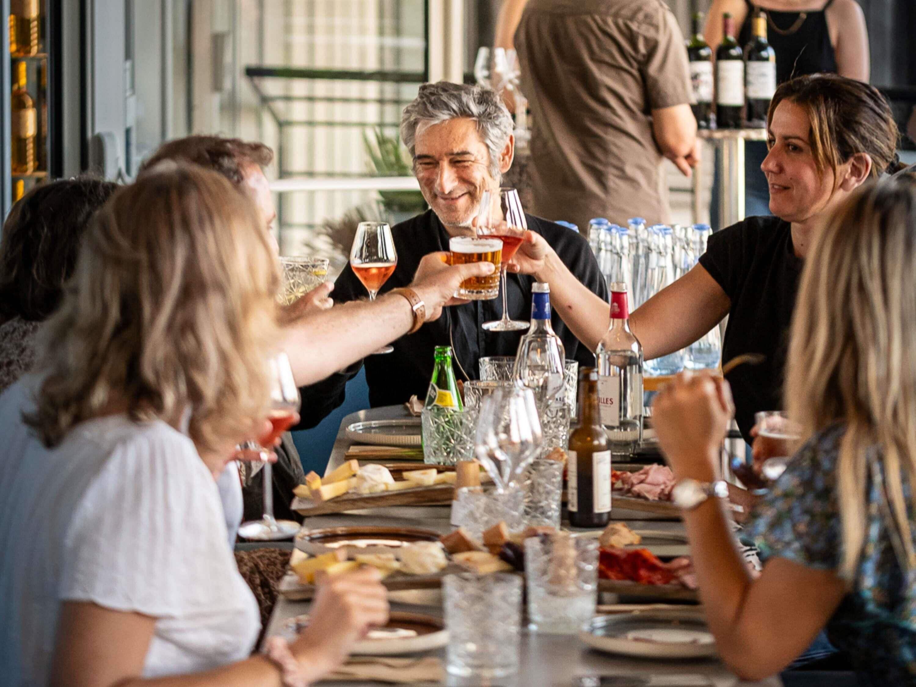 Un groupe de personnes trinquant autour d’une table, avec différents verres et bouteilles, ce qui laisse supposer qu’il s’agit d’une réunion sociale ou d’une célébration.