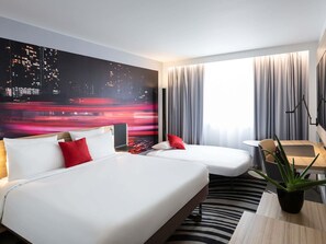 A hotel room with a bed, a desk, a chair, a plant, and a cityscape mural on the wall. - Novotel Bordeaux Centre-Ville (Bordeaux)