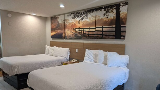 Two single beds with white bedding, a wooden headboard, and a large landscape painting above.