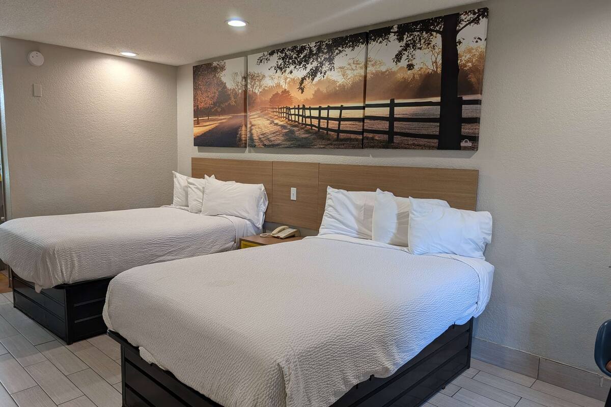 Two single beds with white bedding, a wooden headboard, and a large landscape painting above.