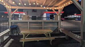 An outdoor seating area with a wooden bench and picnic table, surrounded by a metal fence.