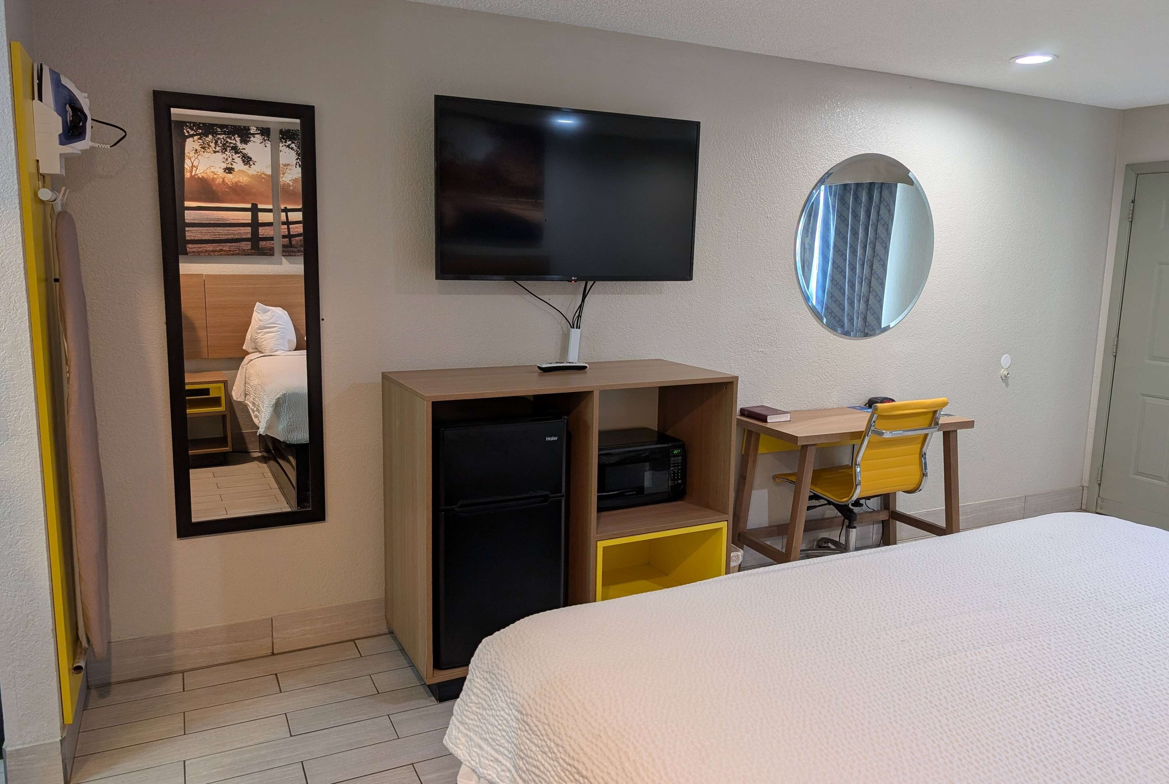 Habitació d'hotel amb un llit, escriptori amb cadira, televisió, nevera i mirall.