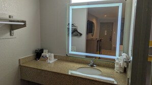 A hotel bathroom with a granite countertop, a sink, a mirror, and a towel rack.