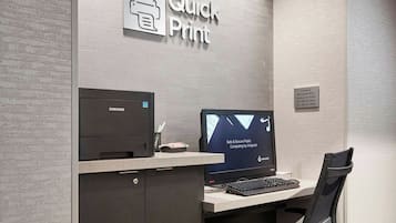 A modern office space with a "Quick Print" sign, a Samsung printer, a monitor displaying a sales and secure public computing interface, and a black office chair.