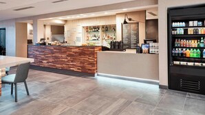 Un hall d’hôtel moderne comprenant un comptoir d’accueil, un espace salon et un distributeur automatique de boissons.