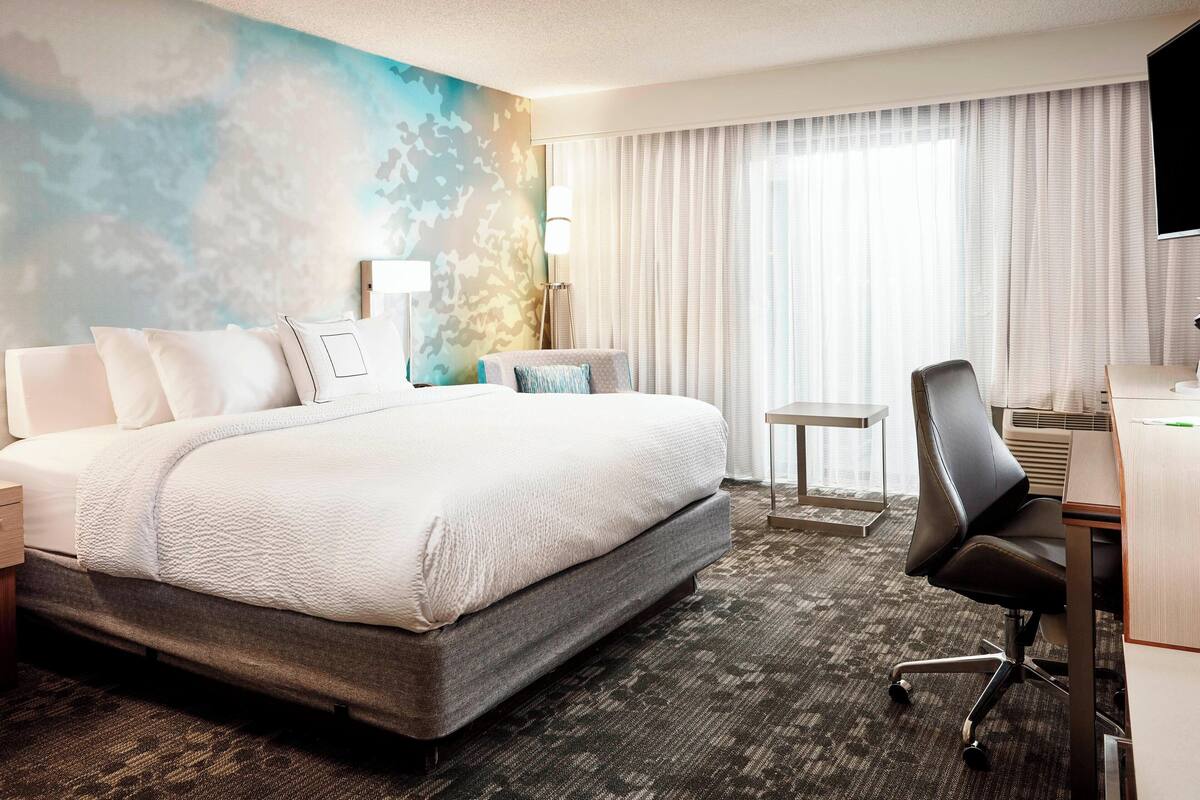 Une chambre d’hôtel avec un grand lit, un bureau avec une chaise, une petite table et un téléviseur.