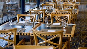 Un restaurant avec de longues tables et des chaises, des lampes orange suspendues et de grandes fenêtres.
