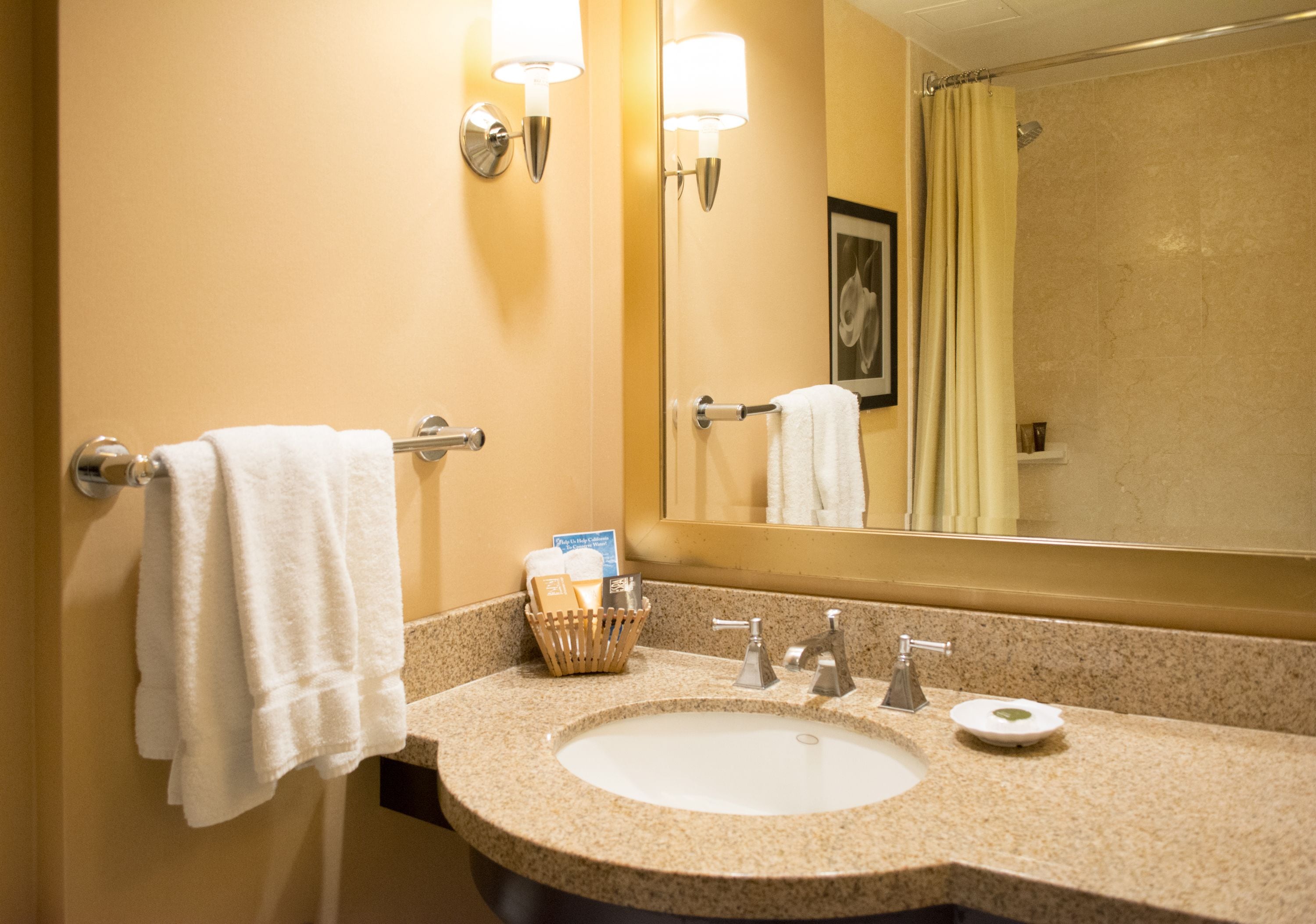 A bathroom with a sink, two wall-mounted lights, a towel rack, a mirror, and a shower curtain.
