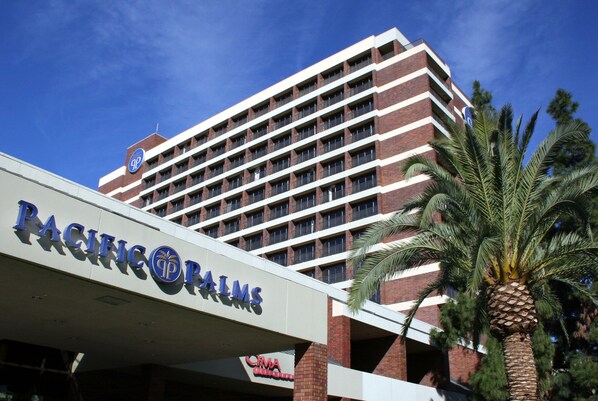 A Pacific Palms hotel with a prominent sign, multiple floors, and a palm tree in the foreground.