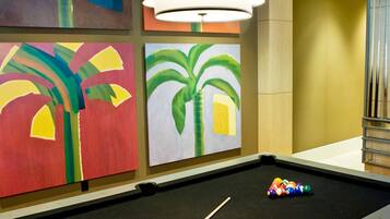 A pool table with a cue stick, surrounded by colorful paintings of palm trees.