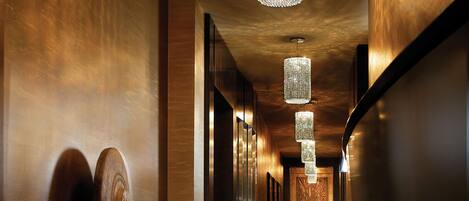 A hallway with a patterned carpet, wooden accents, and hanging crystal chandeliers.