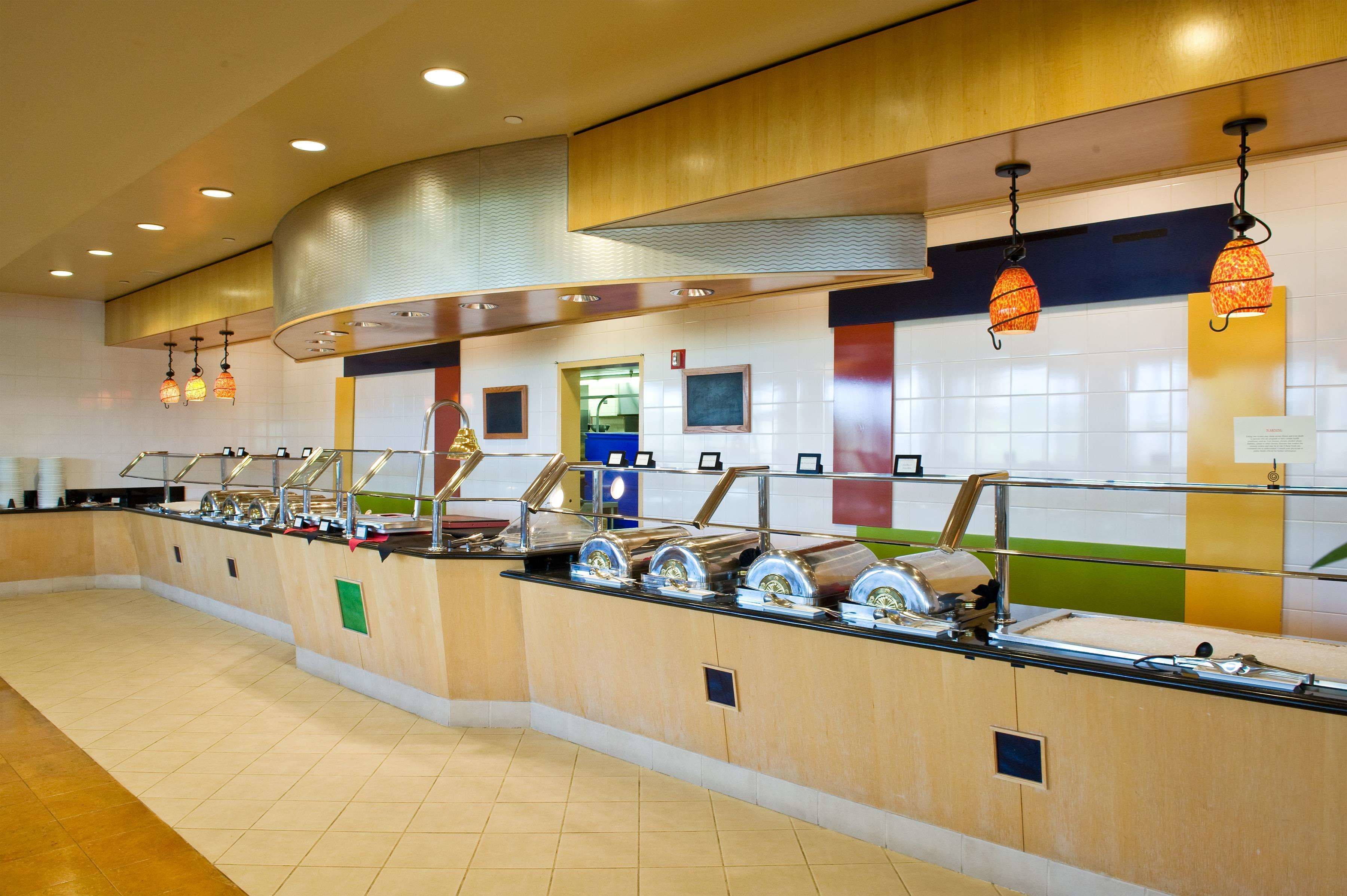 A buffet area with multiple food dispensers, a ventilation hood, and a tiled wall with colorful accents.