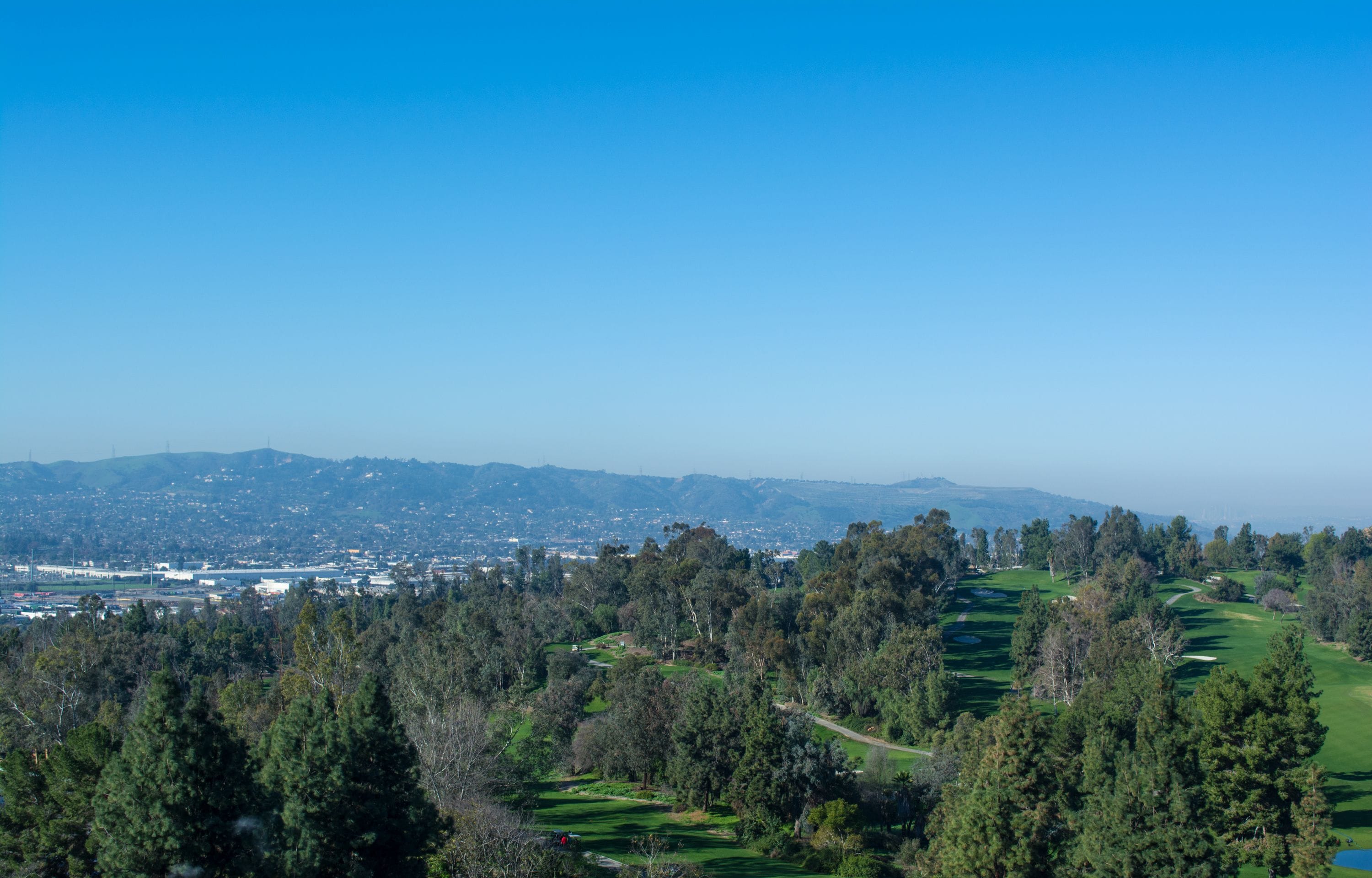 Ein weitreichender Blick auf einen Golfplatz, im Hintergrund eine Stadt.