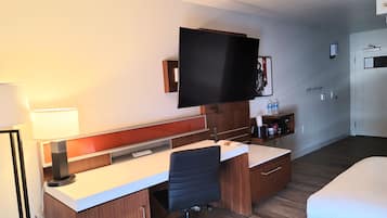 Een hotelkamer met een bureau, stoel, bed, televisie en een klein plankje met toiletartikelen.