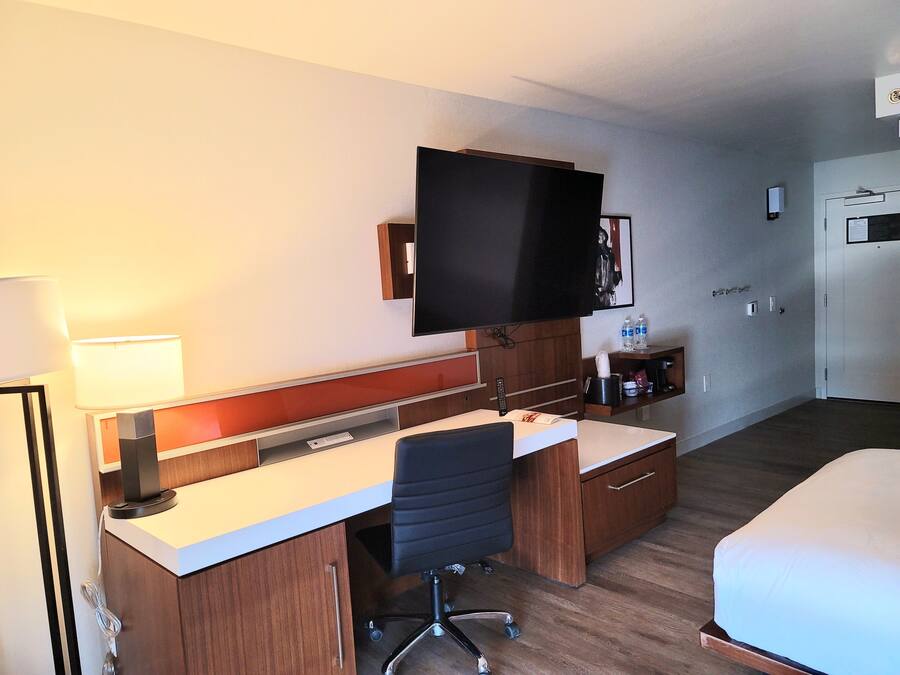 Een hotelkamer met een bureau, stoel, bed, televisie en een klein plankje met toiletartikelen.