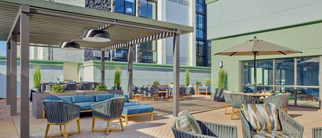Un espace extérieur aménagé en terrasse, avec des coins salon comprenant des canapés et des fauteuils, ainsi qu’une partie couverte avec des parasols.