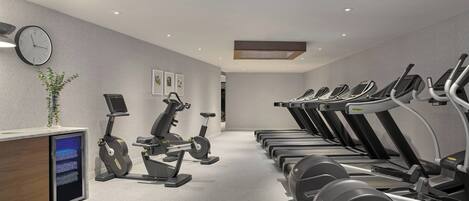 A gym with multiple treadmills, a wall clock, and a digital display on a cabinet.
