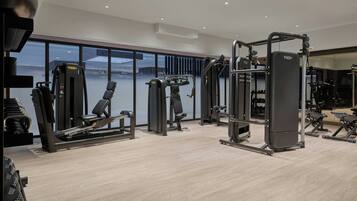 Ett modernt gym med olika träningsmaskiner, stora fönster och ett trägolv.