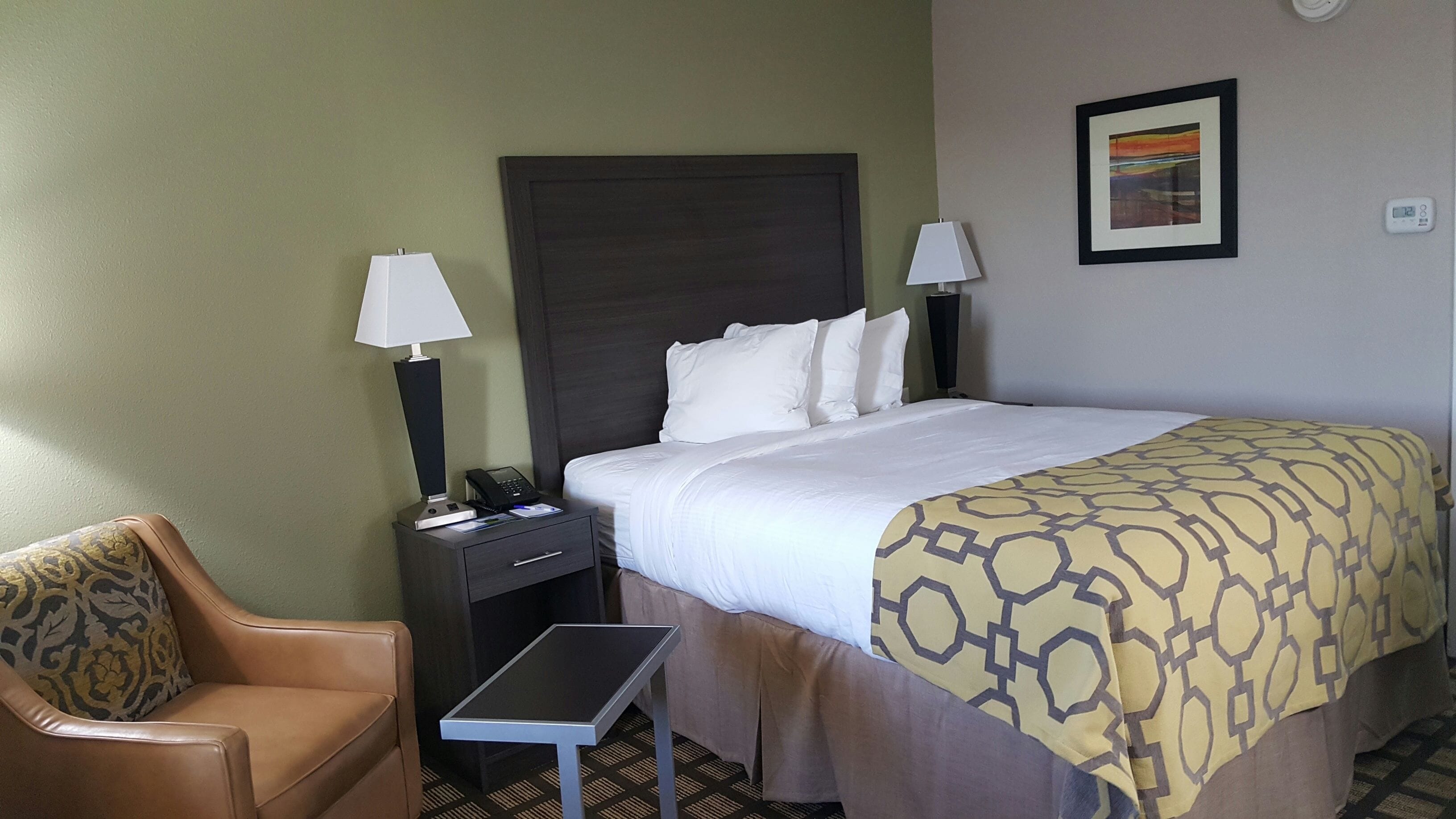 Une chambre d’hôtel avec un lit, des lampes de chevet, un bureau avec un téléphone, une chaise et une petite table.